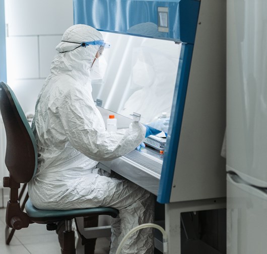Technicien en combinaison de protection intégrale manipulant un échantillon sous hotte de biosécurité, laboratoire modulaire Kum Concept